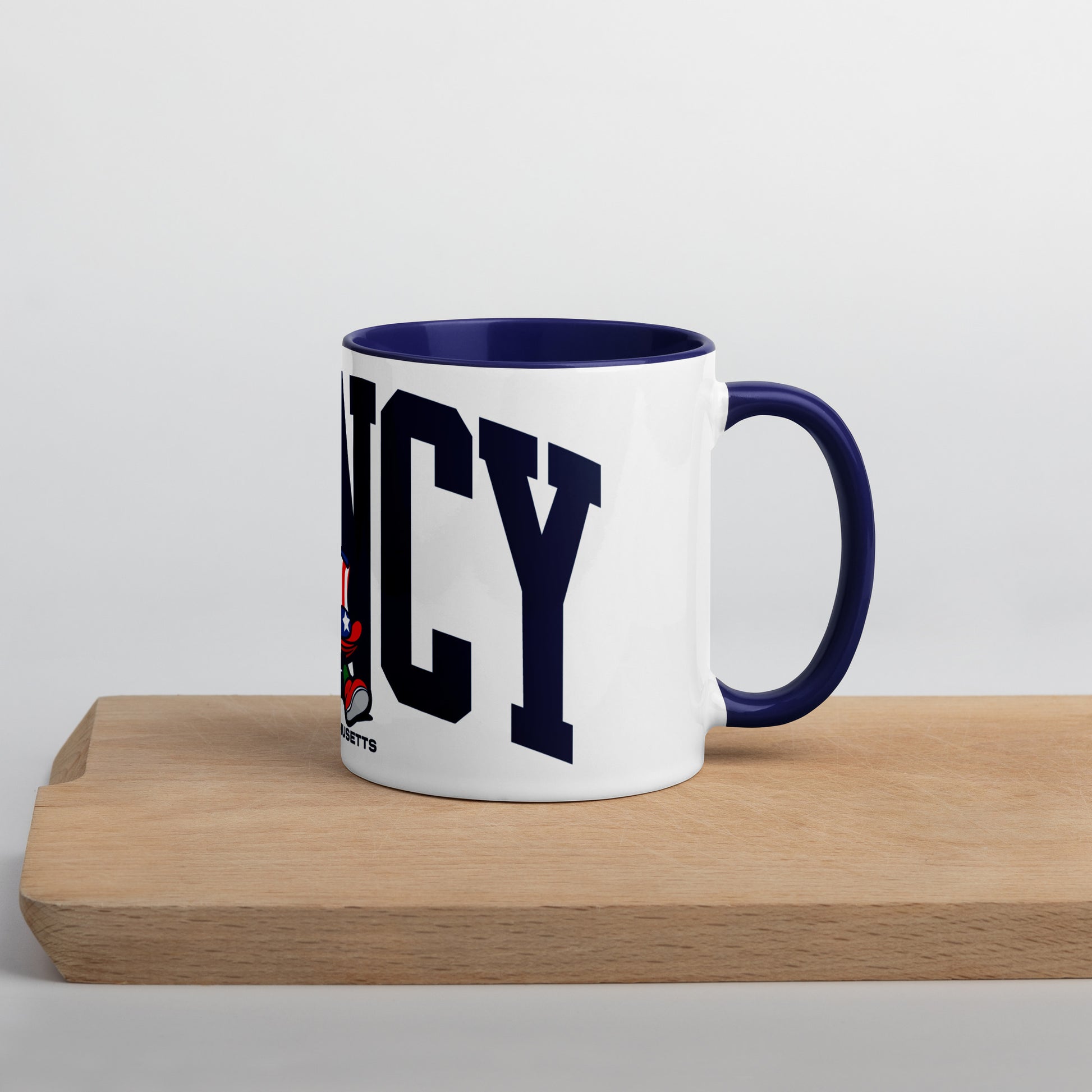 A white ceramic mug with a navy blue interior and handle, featuring bold navy letters spelling “QUINCY” across the front. In front of the text is a cartoon-style Walking President character wearing a red, white, and blue top hat and red shoes. The word “Massachusetts” appears below the artwork. The mug sits on a light wooden surface with a soft gray background.