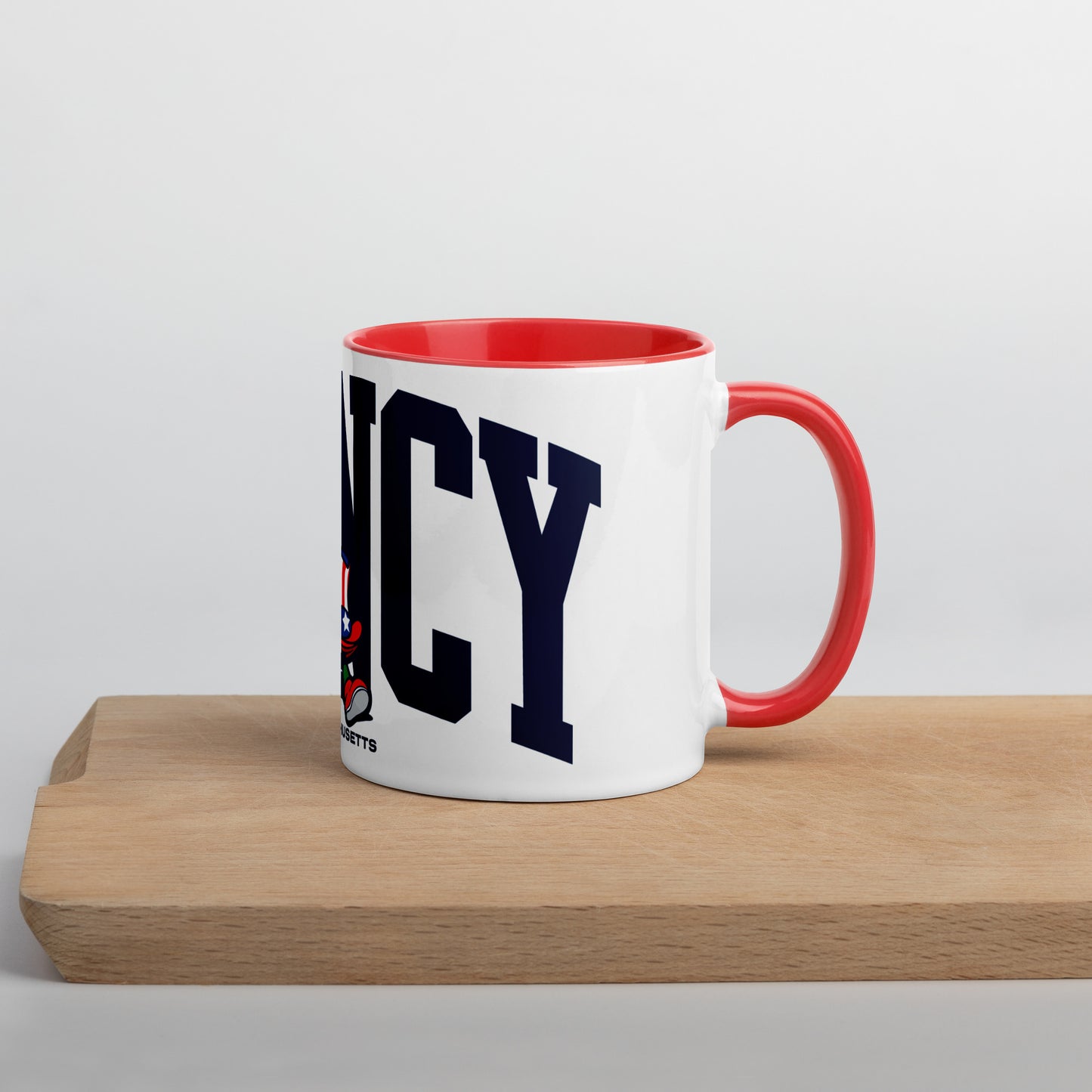 A white ceramic mug with a red interior and handle, featuring bold navy letters spelling “QUINCY” across the front. In front of the text is a cartoon-style Walking President character wearing a red, white, and blue top hat and red shoes. The word “Massachusetts” appears below the artwork. The mug sits on a light wooden surface with a soft gray background.